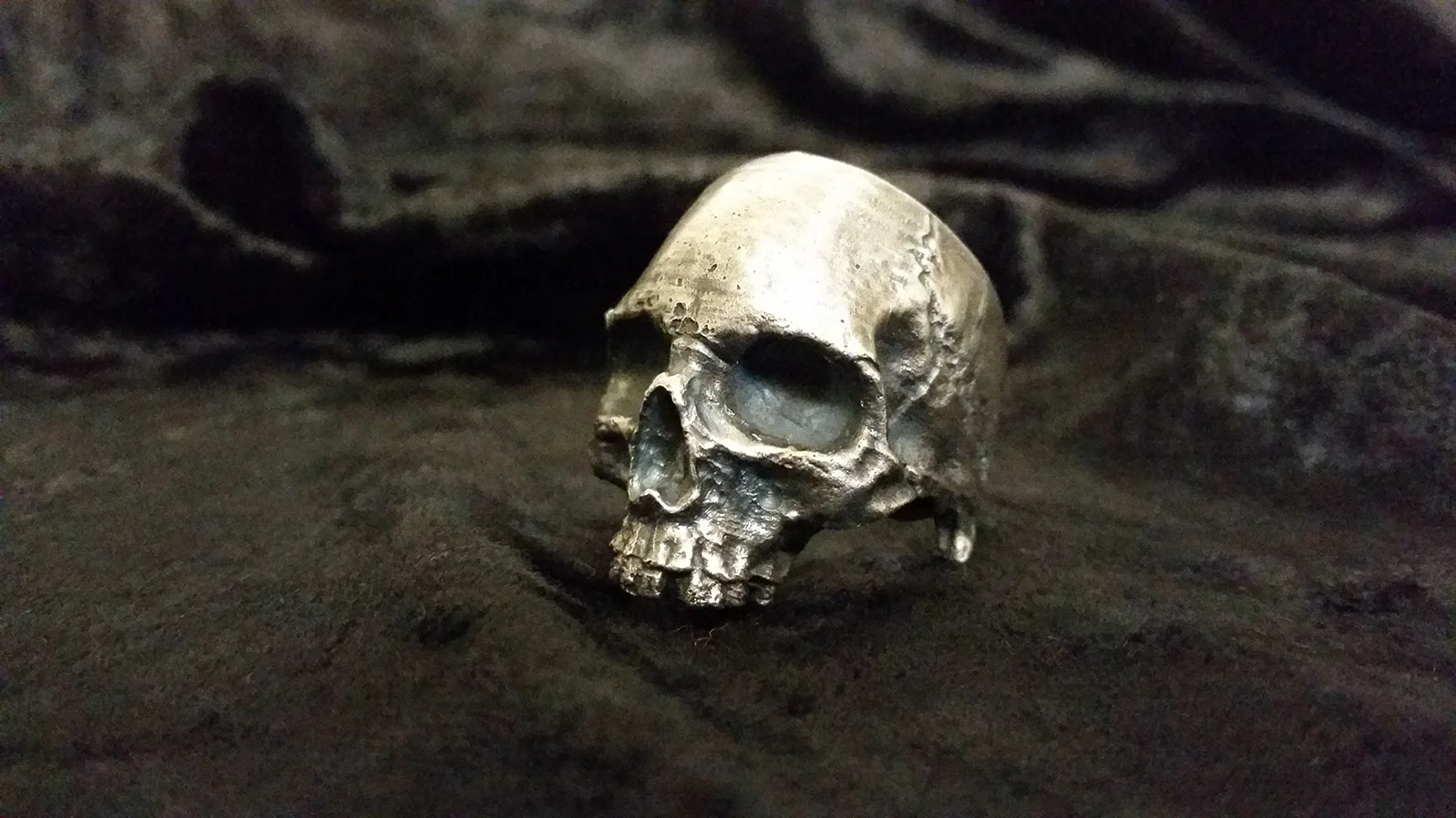 Bague en forme de crâne réalisée par fonte à la cire perdue, sur un tissu sombre